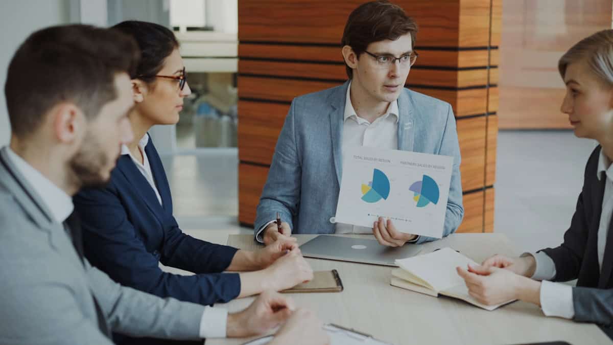 Equipe discutindo gráficos em reunião, ilustrando a escolha entre os tipos de importação: direta, conta e ordem e encomenda